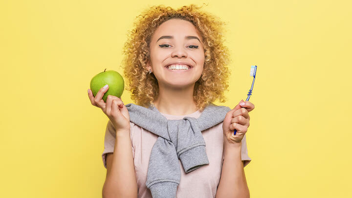 A woman smiling holding an apple and a tooth brush